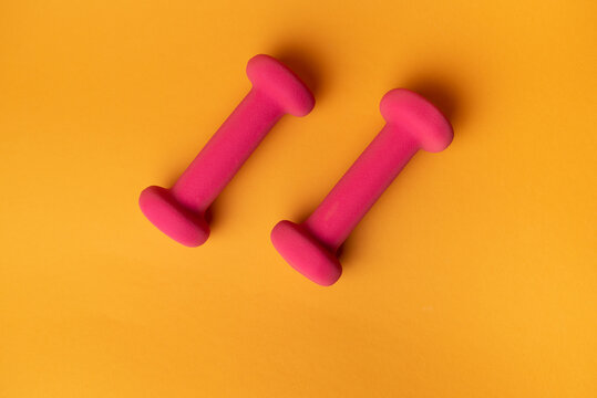 two pink dumbbells for fitness on yellow background © Pavel