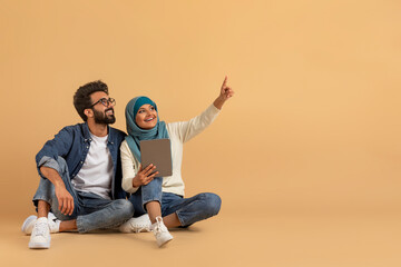Excited young muslim couple holding digital tablet and pointing at copy space