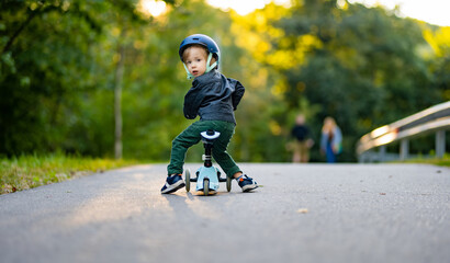 Funny toddler boy riding a baby scooter outdoors on autumn day. Kid training balance on mini bike...