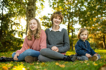 Two big sisters and their toddler brother having fun outdoors. Two young girls with a toddler boy on autumn day. Children with large age gap. Big age difference between siblings.