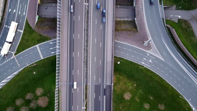 Topdown dronefootage of a mayor roundabout combining local roadways with up and off ramps to/from the highway. The dronecamera is facing downwards and slowly moving upwards the screen.