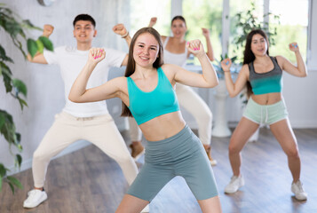 Female teenager performs movements during warm-up, limbering-up part of workout together with peers. Group of young girls and guy engage modern waacking dance in fitness club.
