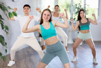 Fototapeta premium Female teenager performs movements during warm-up, limbering-up part of workout together with peers. Group of young girls and guy engage modern waacking dance in fitness club.