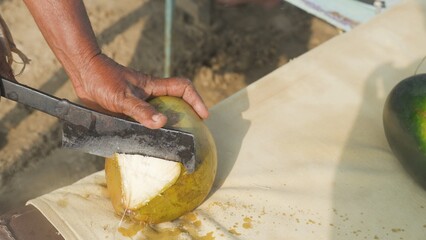 coconut vendor prepares a coconut for drinking using a large knife