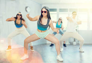 Positive emotional brunette girl performing krump movements with group in modern dance studio.Form...
