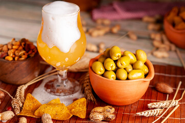 glass of blonde beer with foam falling with peanuts and green olives and snack