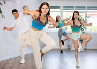 Fototapeta na wymiar Positive female teenager dances groove in choreographic school, group of young people in sportswear trains together with their classmates in gym before competitions, battle