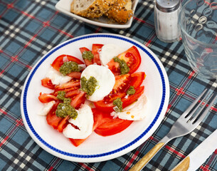 Caprese salad of tomato and mozzarella with balsamic glaze dished up in a plate on the laid restaurant table