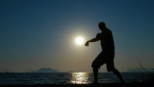 Sporty man silhouette on empty shore. A sporty man silhouette practising shadow boxing on the empty beach during nightfall. A concept of sporty people evenings.