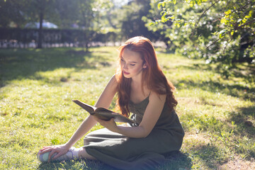 very beautiful freckled white woman with long red hair reading in a garden