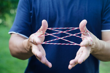 Closeup man hands is playing rope which called cats cradle game. Concept, game involving the creation of various style figures between the fingers. Traditonal playing. - obrazy, fototapety, plakaty