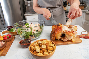 woman prepares a caesar salad in the kitchen. Pieces of fried chicken are added to the salad bowl. Knife and hands close-up.