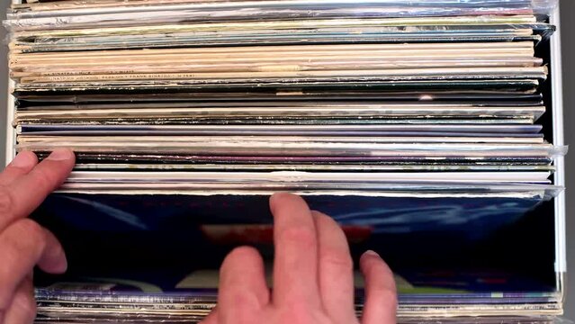 male music lover flips through a stack of vinyl records in a music store. Close-up.