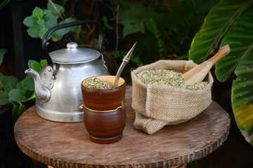 Mate argentino mas pava de acero y bolsa con yerba mate sobre una mesa rústica. Compartiendo un mate en el jardín © Daniel