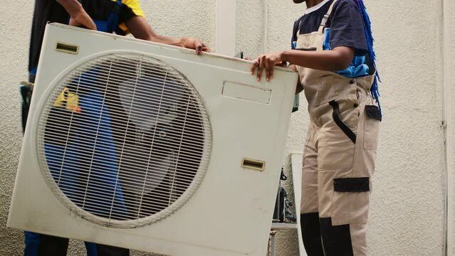 Knowleadgeable engineer and efficient technician opening up old faulty hvac system, to replace it with new performant outside air conditioner after draining freon and replacing ductwork.