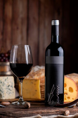 glass of red wine with bottle serving the glass on table with board of various cheeses country...