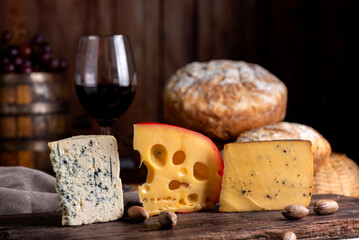 glass of red wine with bottle serving the glass on table with board of various cheeses country bread nuts with wooden background