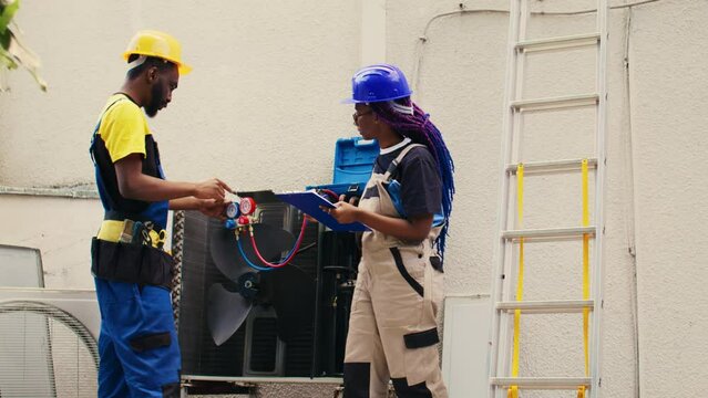 Diverse team of capable electricians brainstorming possible ways to repair damaged outdoor hvac system. Seasoned wiremen colleagues commissioned to fix broken air conditioner