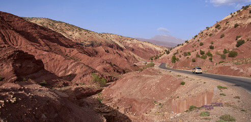 Winding asphalt mountain road crossing red Moroccan soil in Atlas mountains, Morocco. Colorful hills and mountain ranges of Atlas mountains. 