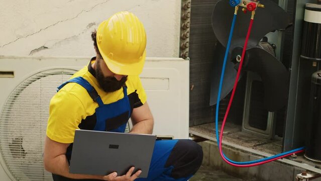 Licensed serviceman using laptop to look online for new evaporator coil after finding external HVAC system malfunctioning internal part during home owner comissioned maintenance