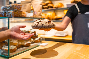 Customer hands in the bakery shop buying an artisan bread from the baker in the workshop workshop