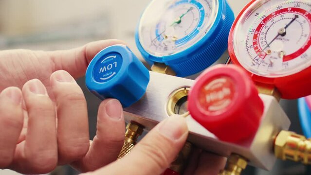 Extreme close up shot of repairman calibrating pressure measurement device during comissioned air conditioner troubleshooting. Worker turning on red and blue superheat and subcooling manometer knobs