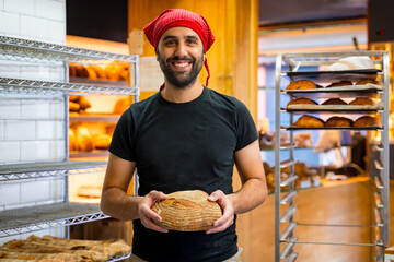 Corporate portrait of smiling bakery manager in the artisan bakery workshop, with a bread in his...