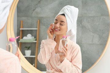 Beautiful woman in terry towel removing makeup with cotton pad near mirror indoors © New Africa
