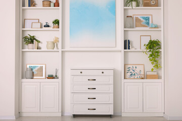 Interior design. Abstract picture and chest of drawers between shelves with accessories indoors