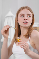Fototapeta premium Young woman with bottle of essential oil in bathroom