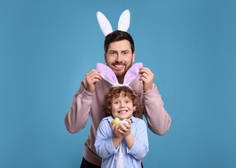 Happy father and son in cute bunny ears having fun on light blue background. Easter celebration