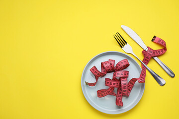 Measuring tape, fork and knife on yellow background, flat lay with space for text. Weight loss concept