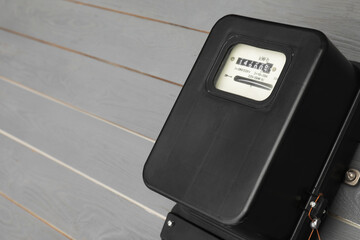 Black electric meter on grey wooden wall, space for text. Measuring device