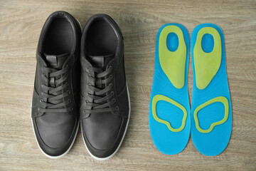 Orthopedic insoles near shoes on floor, flat lay