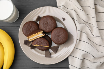 Tasty banana choco pies, pieces of chocolate, milk and fruits on grey wooden table, flat lay