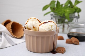 Scoops of ice cream with caramel sauce and candies on light grey table, closeup