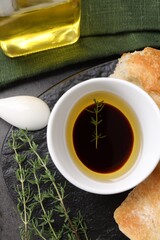 Bowl of organic balsamic vinegar with oil, thyme and bread on grey table, flat lay