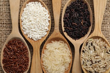 Spoons with different sorts of rice on burlap fabric, flat lay