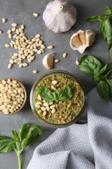 Jar of delicious pesto sauce and ingredients on grey table, flat lay