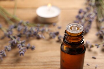 Bottle of essential oil and lavender flowers on wooden table, closeup. Space for text