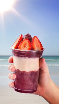 Hand holding a cup of a&ccedil;a&iacute; on the beach