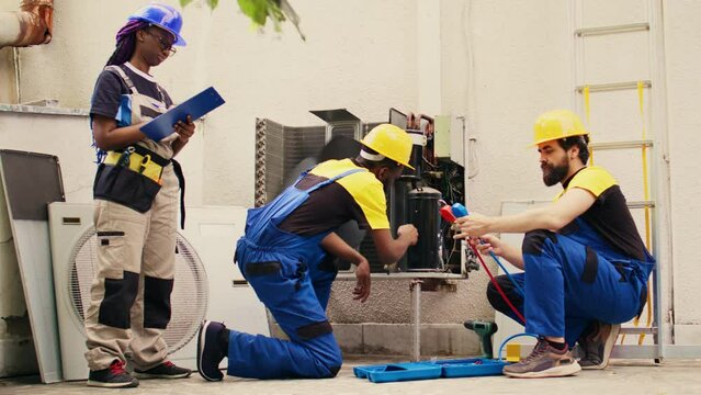 Competent mechanic cleaning layer of dirt and dust from condenser compressor coils while coworker uses measurement device to check for refrigerant leaks. read pressure in hvac system.
