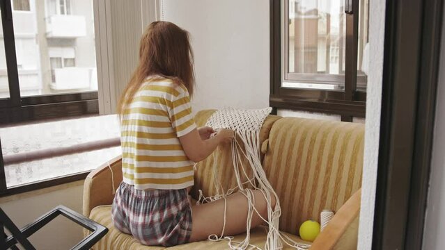 A woman is engaged in weaving macrame at home
