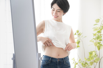 Fototapeta na wymiar ダイエット成功などの明るいイメージの女性　鏡でお腹周りやウエストを確認する