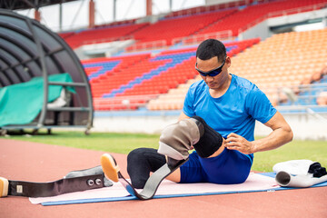 Asian para-athlete with prosthetic blades stretching leg in stadium.