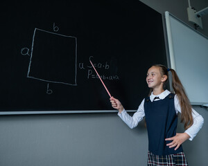 The schoolgirl answers at the lesson. Caucasian girl writes a formula on a blackboard.