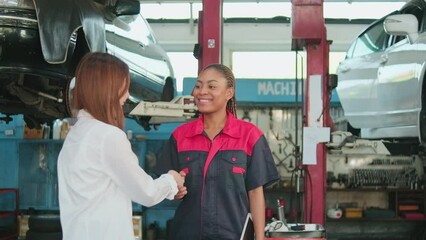 An Asian female customer receives car key and handshakes with automotive worker with happy smile with trust at maintenance garage, professional vehicle service center, fix checks, and repair industry.