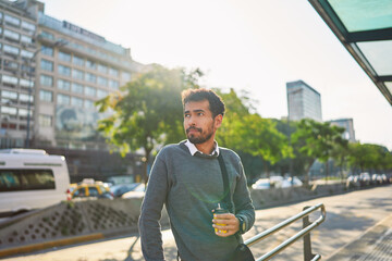 Latin American young adult man on the street of the bus stop waiting for public transportation in...