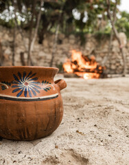 Traditional painted Maya ceramic in tropical sandy garden with bonfire and white wall in the background in Tulum on a cloudy day 