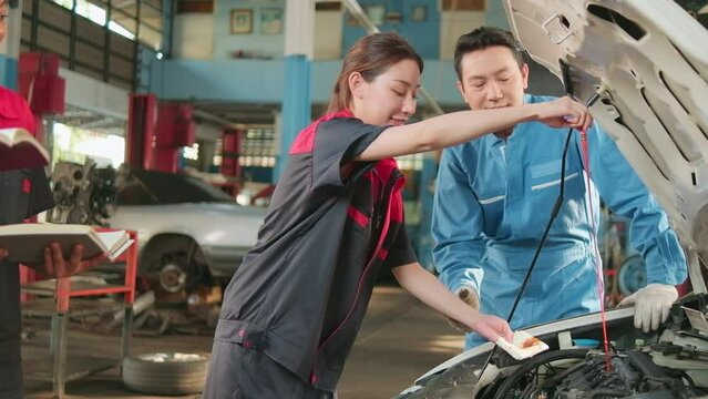 Asian male professional automotive supervisor advises and inspects a mechanic worker woman about liquid engine oil at car garage, service maintenance, and fix specialist occupations auto industry.